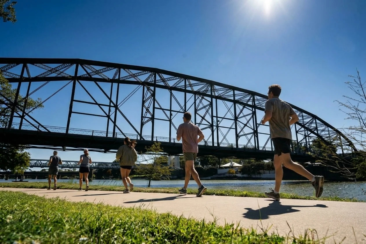 Runners following a riverside path beneath a steel bridge in Waco
